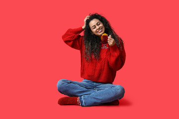 Sticker - Happy young African-American woman with glass cup of hot mulled wine on red background