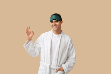 Canvas Print - Portrait of handsome young man in bathrobe and sleeping mask showing OK on beige background