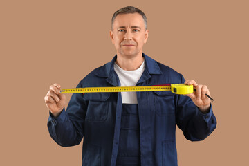 Wall Mural - Male construction worker with measuring tape on brown background