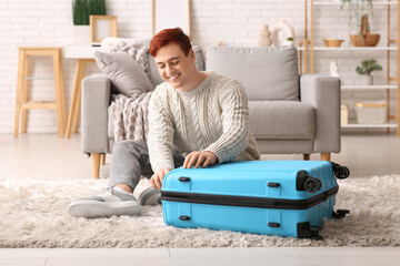 Wall Mural - Happy young man with stylish suitcase sitting on floor at home