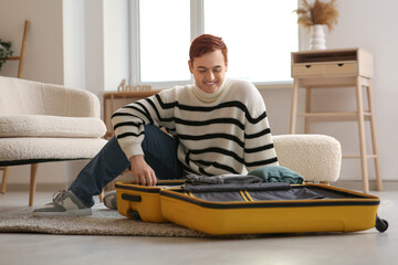 Wall Mural - Young man packing suitcase for journey at home