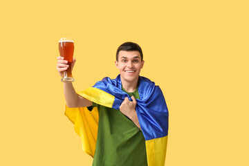 Poster - Young man with flag of Ukraine and glass of beer on yellow background