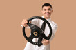 © Pixel-Shot - Young man with steering wheel on brown background