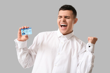 Poster - Young happy man with driver license on grey background