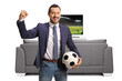 © Ljupco Smokovski - Cheerful man holding a football and gesturing win in front of a tv and sofa