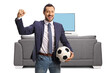 © Ljupco Smokovski - Cheerful man holding a football and gesturing win in front of a tv and couch