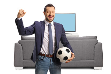 Wall Mural - Cheerful man holding a football and gesturing win in front of a tv and couch