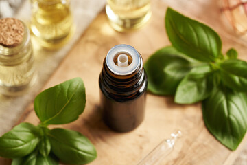 Wall Mural - A bottle of aromatherapy essential oil with fresh basil leaves on a table