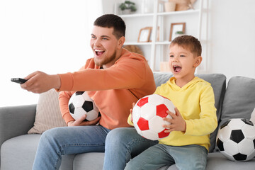 Poster - Young man and his little son with soccer balls emotionally watching football game in living room