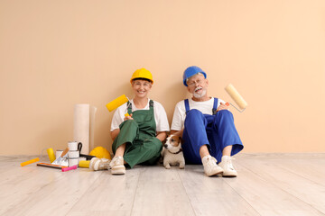 Poster - Mature couple of decorators with dog and paint tools sitting near beige wall