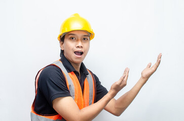 asian man consrtruction worker wearing yellow safety helmet and orange vest smiling and pointing finger to copy space with happy and surprised expression.