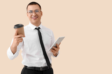 Wall Mural - Handsome businessman with tablet computer and coffee cup on beige background