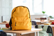 © Pixel-Shot - Yellow backpack with apple and copybooks on desk in classroom