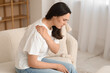 © Pixel-Shot - Young woman suffering from pain in shoulder on sofa at home