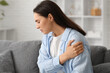© Pixel-Shot - Young woman suffering from pain in shoulder at home