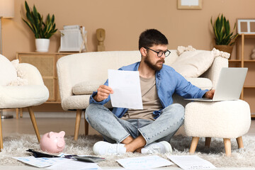 Wall Mural - Young man in debt with paper using laptop at home