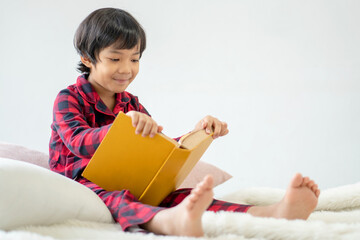 Education and back to school concept. Portrait of Happy little cute child boy in pajamas learning to read a book on the floor. Preschool children kids enjoy and fun study and doing homework at home.