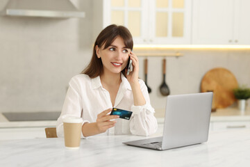 Wall Mural - Online banking. Smiling woman with credit card talking by smartphone at table indoors