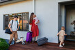 © Austockphoto - Toddler boy helping family carry suitcase of luggage inside at holiday house destination
