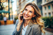 © thanakrit - Smiling woman talking on the phone outdoors, wearing a blazer, with a joyful expression, capturing a moment of positive communication.