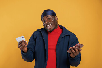 Wall Mural - Credit card and smartphone in hands, making payment. Handsome black man is in the studio against yellow background