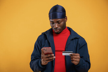 Wall Mural - Credit card and smartphone in hands, making payment. Handsome black man is in the studio against yellow background