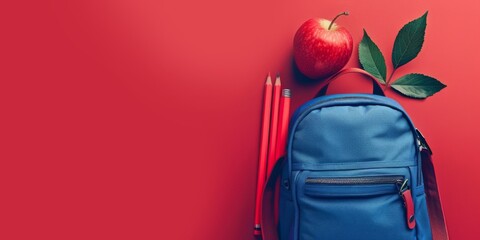 Wall Mural - A blue backpack with a red apple and two pencils on a red background