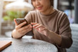© bongkarn - A cropped image of an Asian woman scrolling on her phone while relaxing at an outdoor table.
