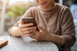 © bongkarn - A cropped image of an Asian woman scrolling on her phone while relaxing at an outdoor table.