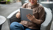 © bongkarn - A cropped image of an Asian woman using her tablet at an outdoor lounge or a cafe in the city.