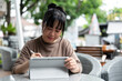 © bongkarn - A happy Asian woman working remotely from a cafe in the city, using her digital tablet.