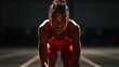 © Nadin Faust - black female track and field runner in red athletic wear, poised at the starting line of an indoor race with soft lighting casting long shadows on her face