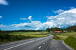© art_of_line - Scandinavian rural landscape, Asphalt road with white markings going through picturesque farmland with farm houses by the forest, Summer sunny day, Västra Götaland County, Sweden