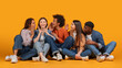 © Prostock-studio - A group of five young adults, including two women and three men of different races, are casually sitting on a bright yellow background. They are all looking at each other, whispering secrets