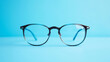 © Volodymyr - Close-up of black eyeglasses with clear lenses on a blue background. Generative AI