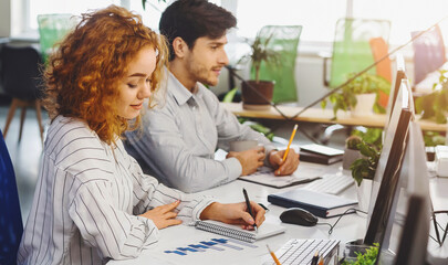 Poster - A man and a woman are seated at a desk, focused on their computer screens. They are engaged in work, typing and clicking on the keyboard and mouse respectively.