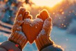 © Bundi - A woman in winter gloves holding a Heart symbol shaped Lifestyle and Feelings concept in front of a sunset-lit background