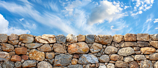 Photograph of a stone wall with a blue sky and clouds background, in the style of copy space concept.


