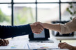 © Wasana - Two people shaking hands in front of a table with papers on it