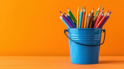 Blue metal bucket with colored pencils for office on an orange background School supplies stationery wide angle lens