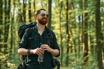 In cool sunglasses. Bearded man is in the forest at daytime