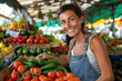 © Alexandra - Greengrocer smiling and choosing a cucumber from a crate full of fresh produce while working in her store at the farmers market