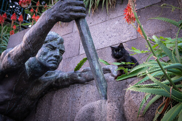 a statue of a man in a park and a sitting cat