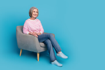 Wall Mural - Full size photo of attractive retired woman sit armchair look empty space dressed stylish striped clothes isolated on blue color background