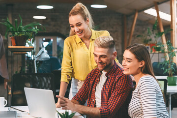 three young colleagues, two women and a man, smile and discuss work while gathered around a laptop i