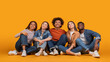 © Prostock-studio - This image features five friends, all wearing casual clothing, sitting on a yellow background. They are looking up, possibly at something interesting or inspiring, with smiles on their faces