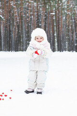 A cute baby in a snowy winter forest. Little girl having fun on winter day. Happy child in winter park.