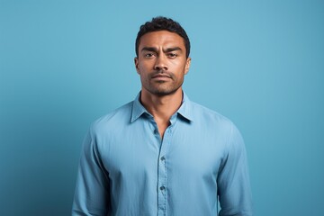 A man in a blue shirt is looking at the camera with a serious expression