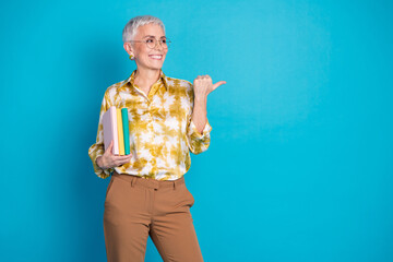 Poster - Photo portrait of lovely pensioner lady point look empty space hold books dressed stylish elegant garment isolated on blue color background