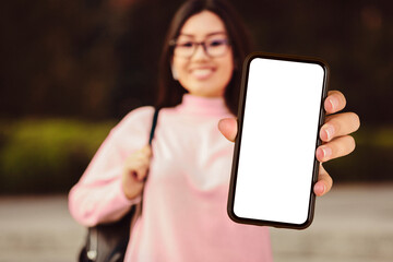 asian woman is holding up a cell phone in her hand, with a blank white screen facing the camera. the